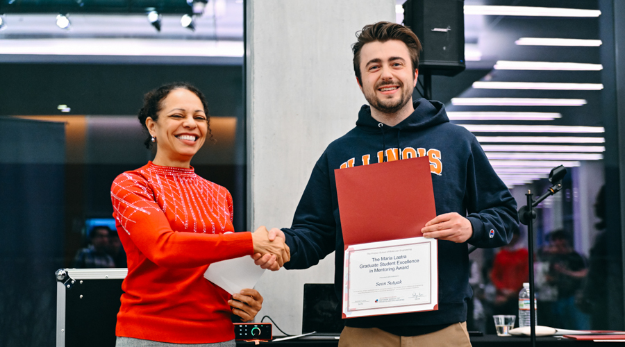 Two scientists stand next to each other, shaking hands for the camera. One is holding an award certificate.