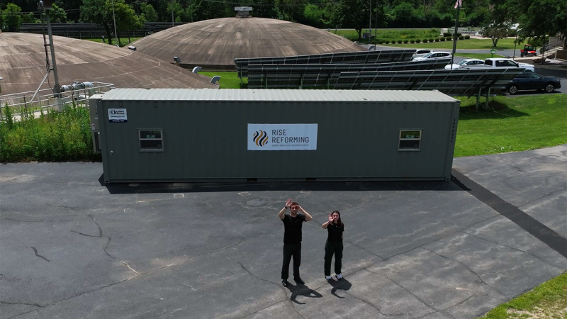 Two people stand in front of a shipping container that says Rise Reforming