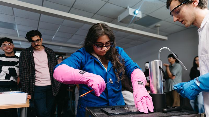 Student wearing pink gloves holds hammer over flat object