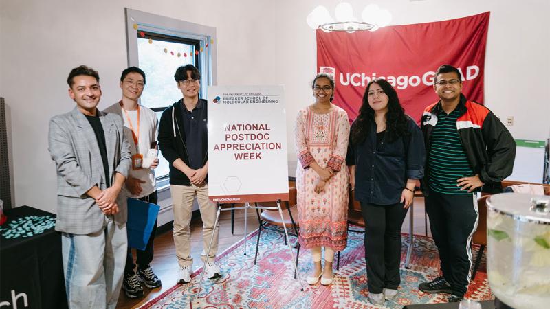 Group of people standing around a sign saying "National Postdoc Appreciation Week"