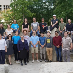 roup photo of the Esser-Kahn Lab Group posing outdoors on stone seating with trees and campus buildings in the background. The image shows researchers and students gathered together for a lab portrait.