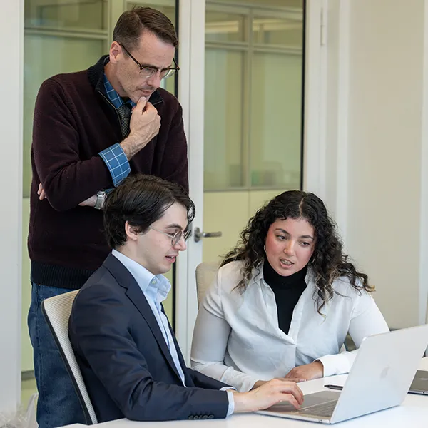 Two students sit at computer while an instructor looks over