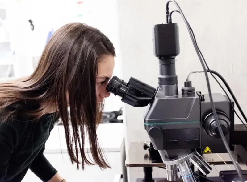 Women with brown long hair looking through microscope