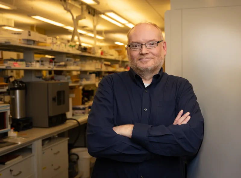 Stuart Rowan, interim dean, standing with arms crossed in a research laboratory.