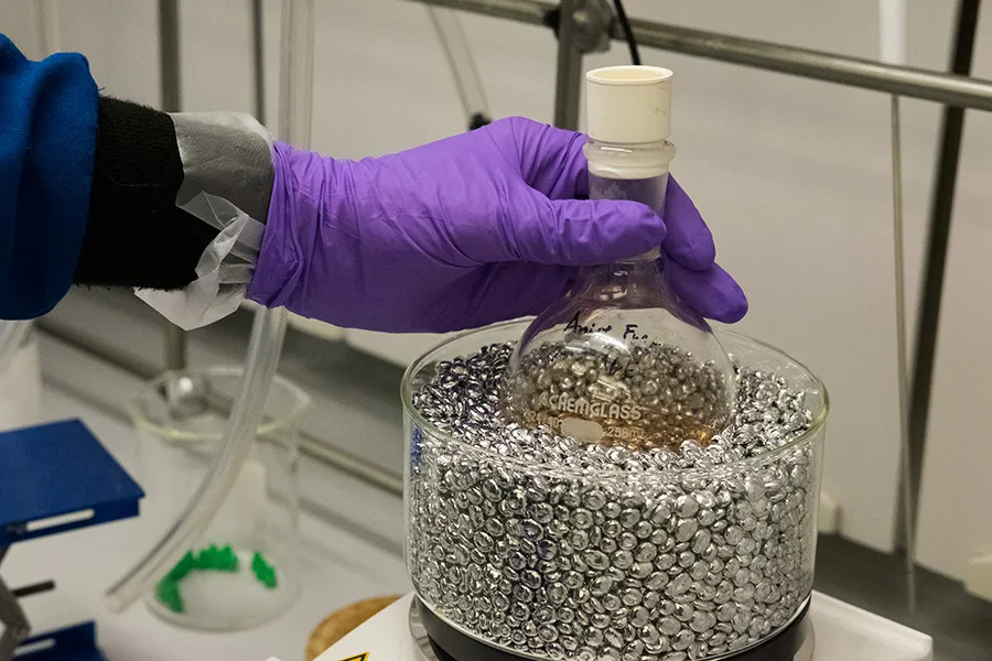 Hand placing a beaker of liquid bottom-first into container with metallic spheres