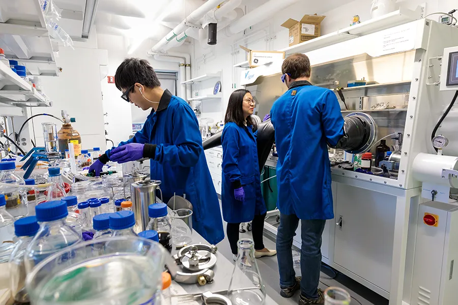 Three researchers wearing blue scrubs performing various tasks in laboratory