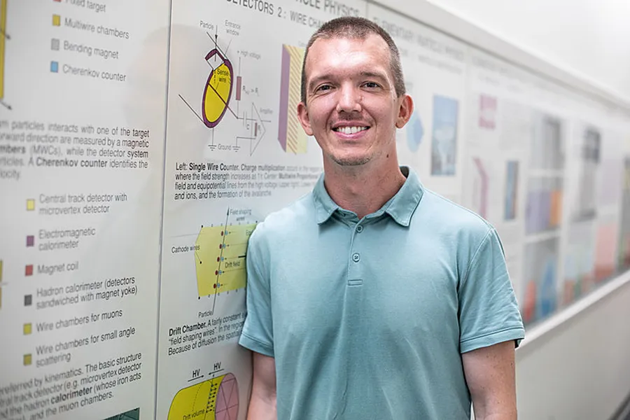 Photo of Zach Sweet in blue polo in front of a row of posters