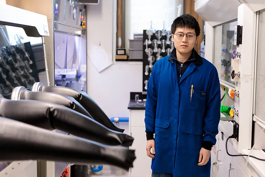 Yahao Dai next to a row of gloveboxes in lab
