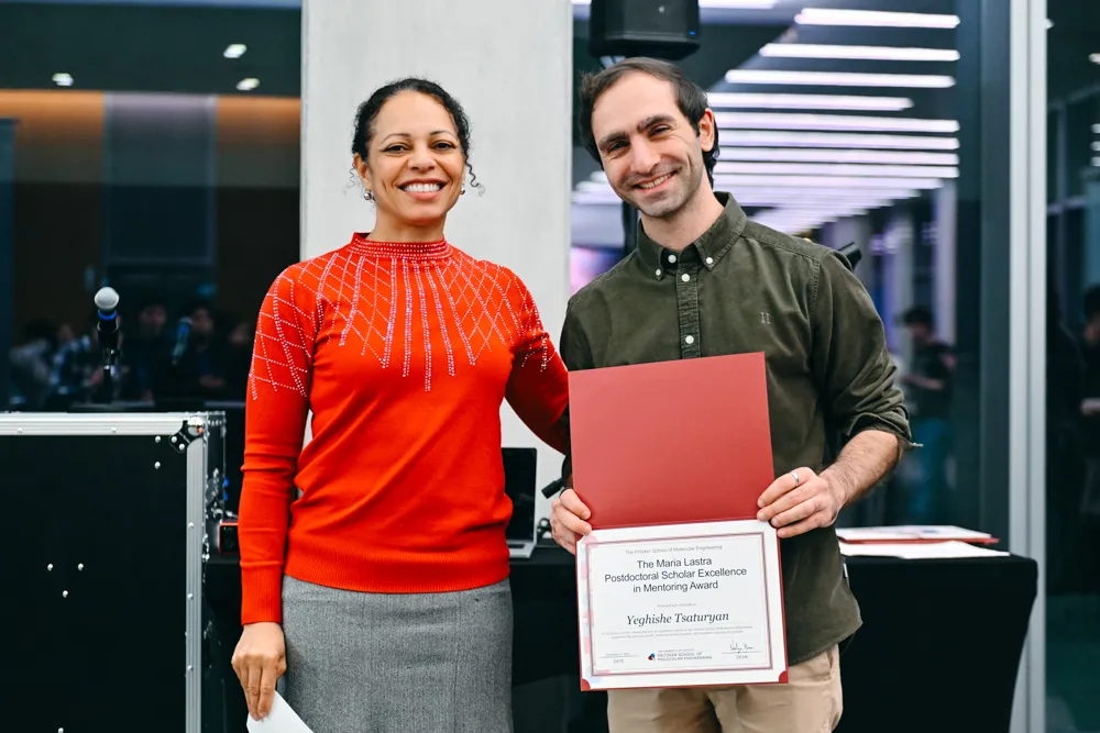 Two scientists stand next to each other, one presenting an award certificate to the other