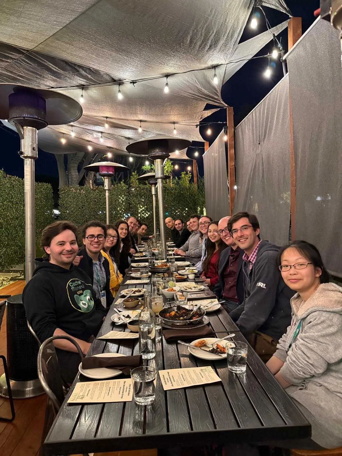 Graduate students and researchers gathered around an outdoor table for a casual group meal on campus.