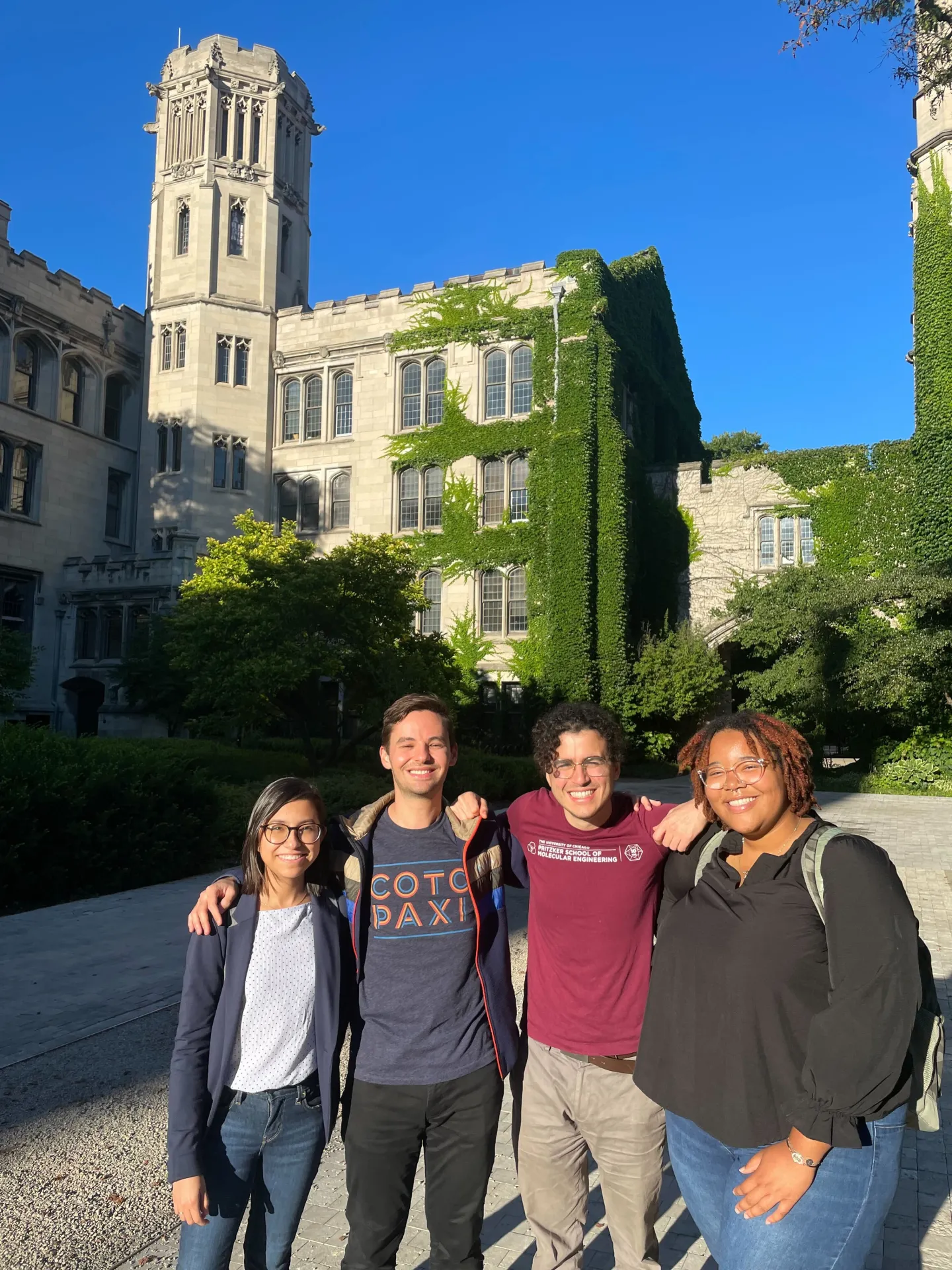 Four students standing together in front of an ivy-covered Gothic-style University of Chicago building.