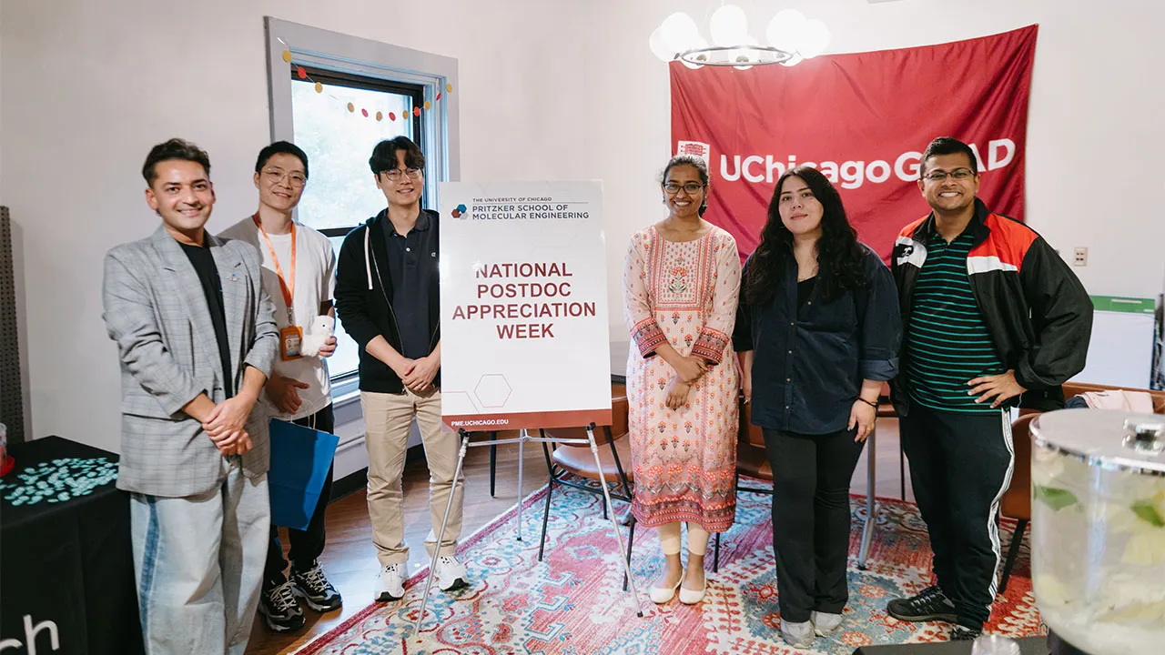 Group of people standing around a sign saying "National Postdoc Appreciation Week"